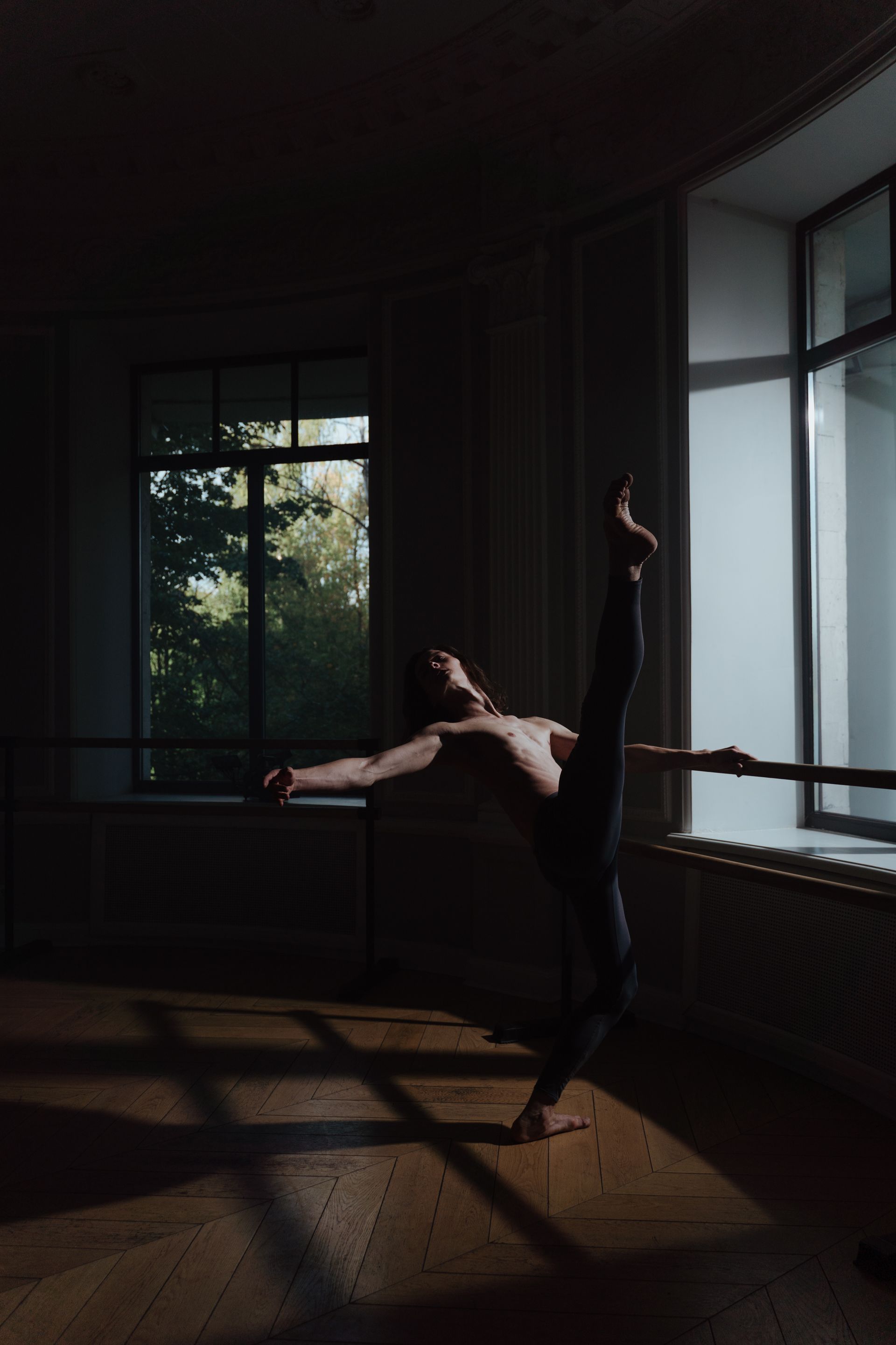 A dancer holding an extended line at the barre in a dark classical studio
