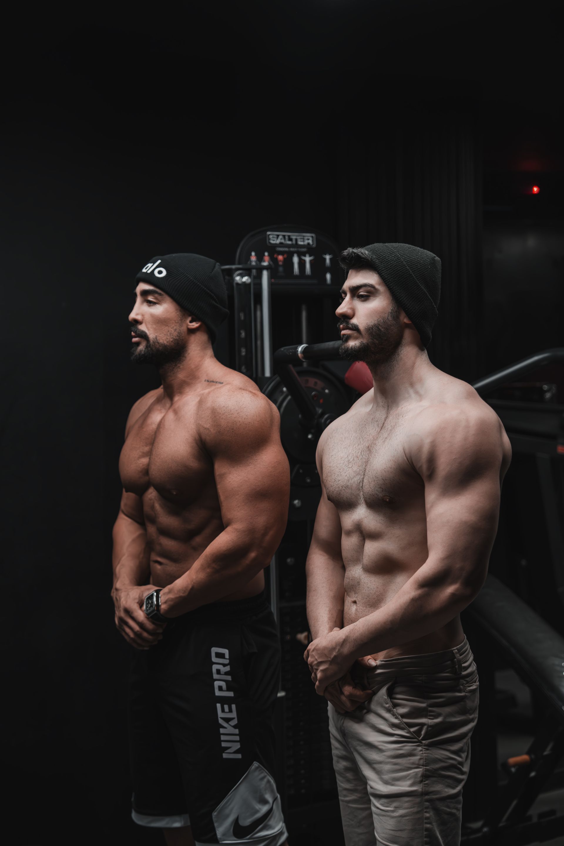 Two physique athletes practicing poses in a dimly lit gym