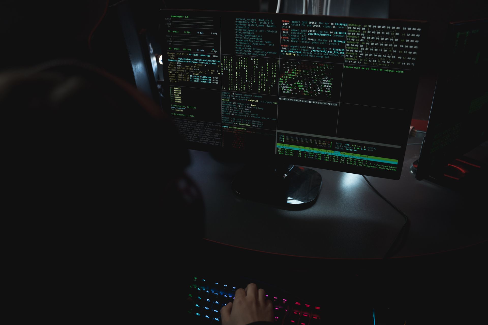 Code running across monitors in a dark room, screen glow the only light