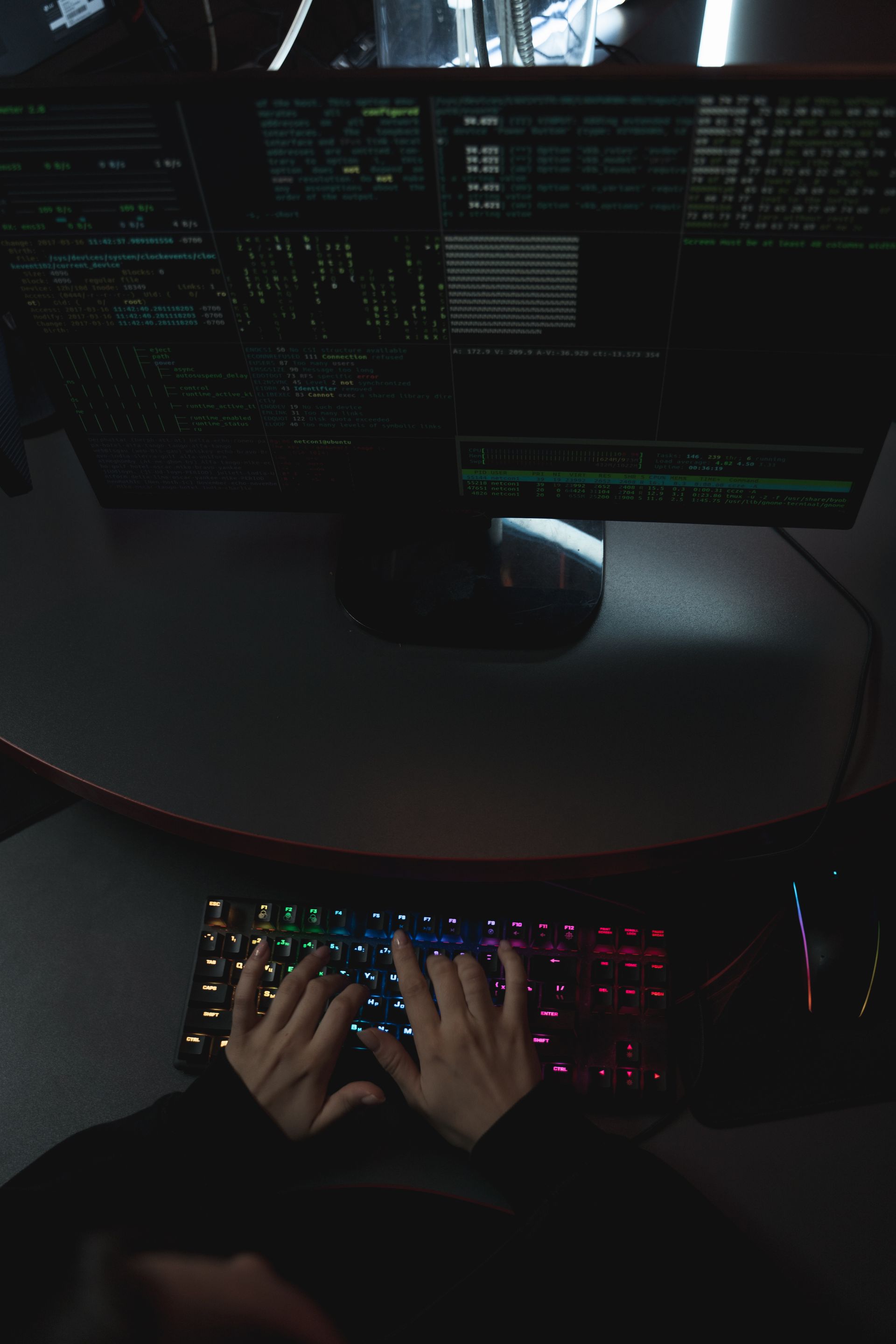Hands on a backlit keyboard with code across dual monitors in a dark room