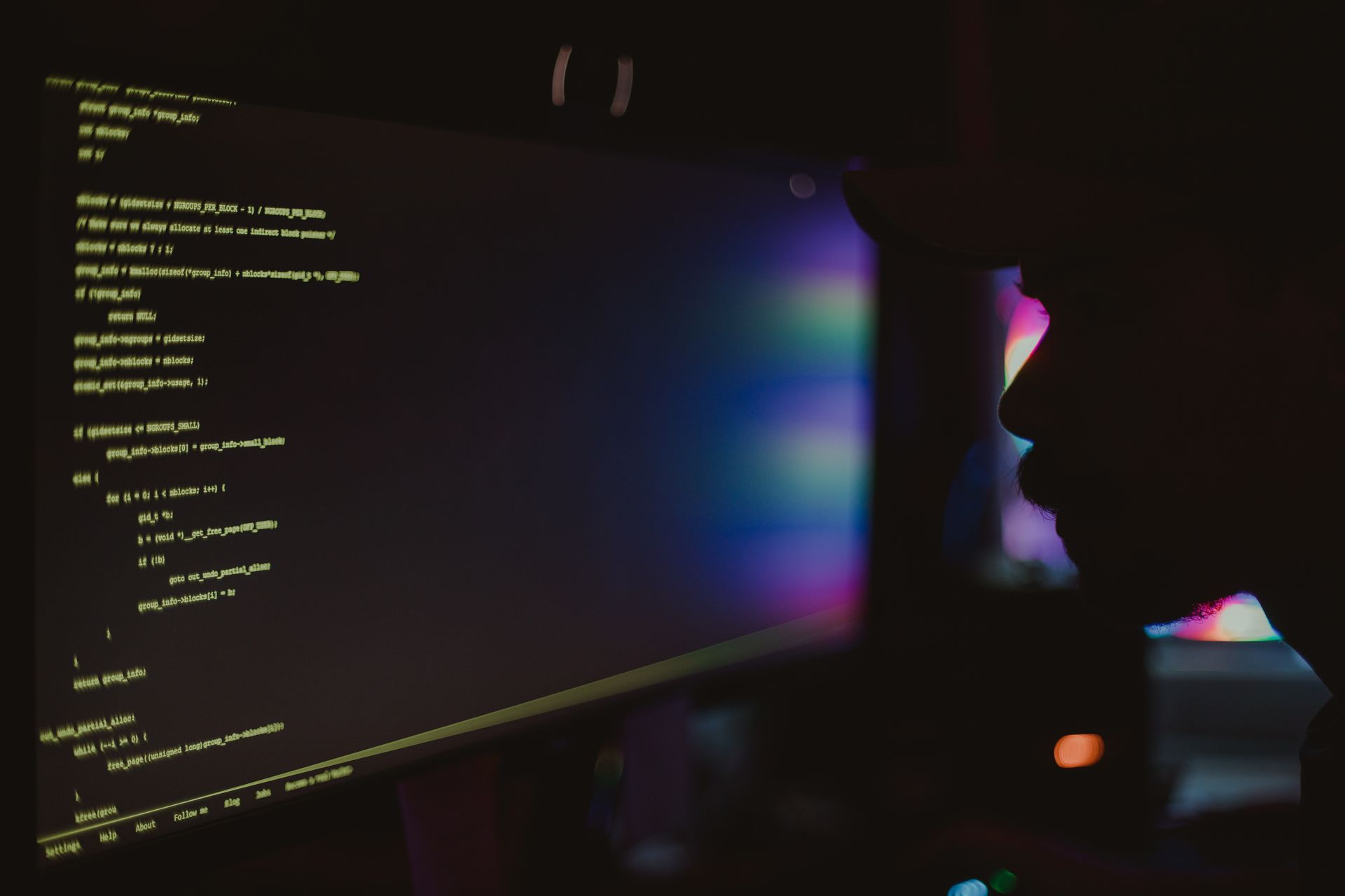 A developer coding at night, silhouetted against a glowing monitor in a dark room