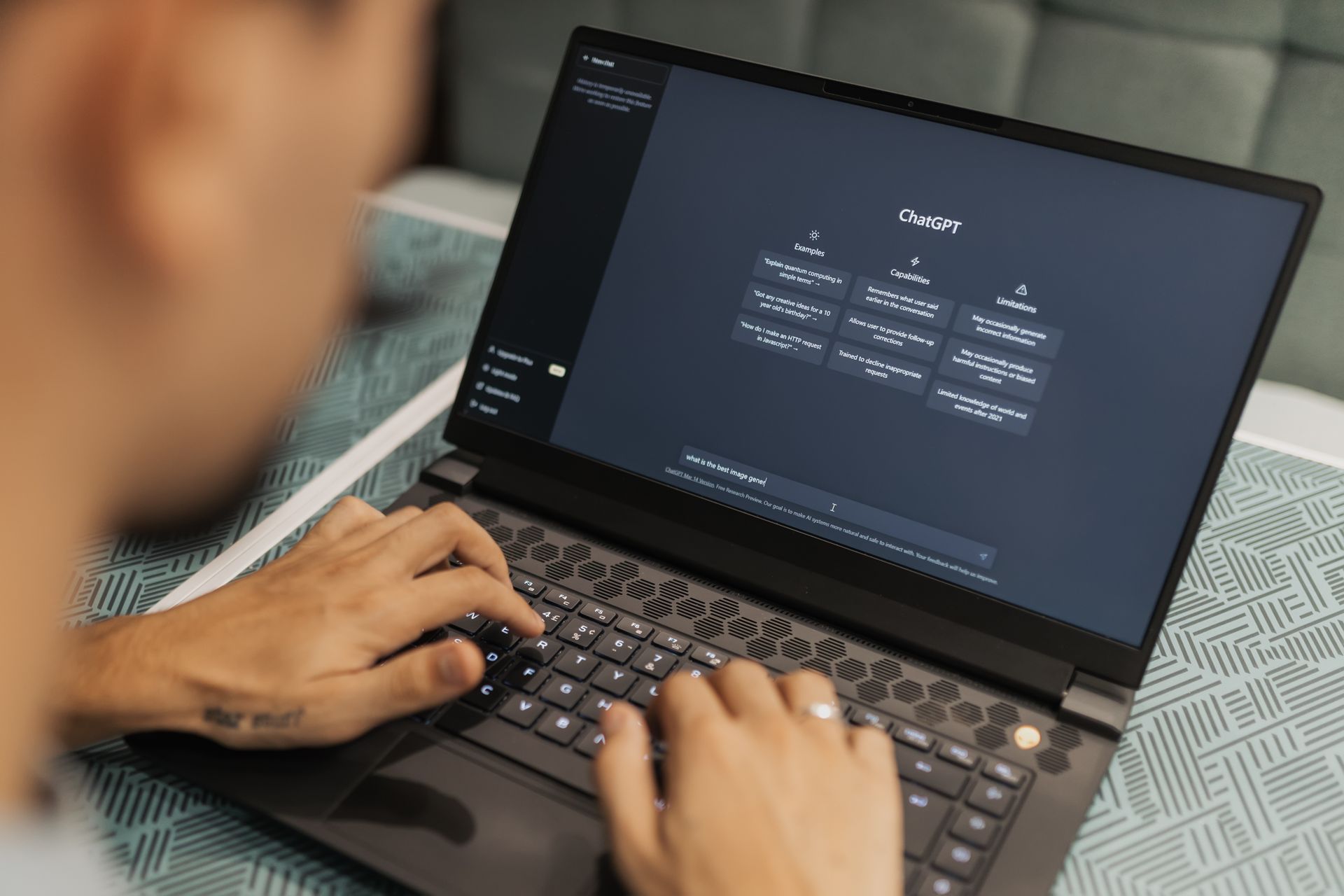 A person working at a laptop with an AI assistant open on screen in a dim room