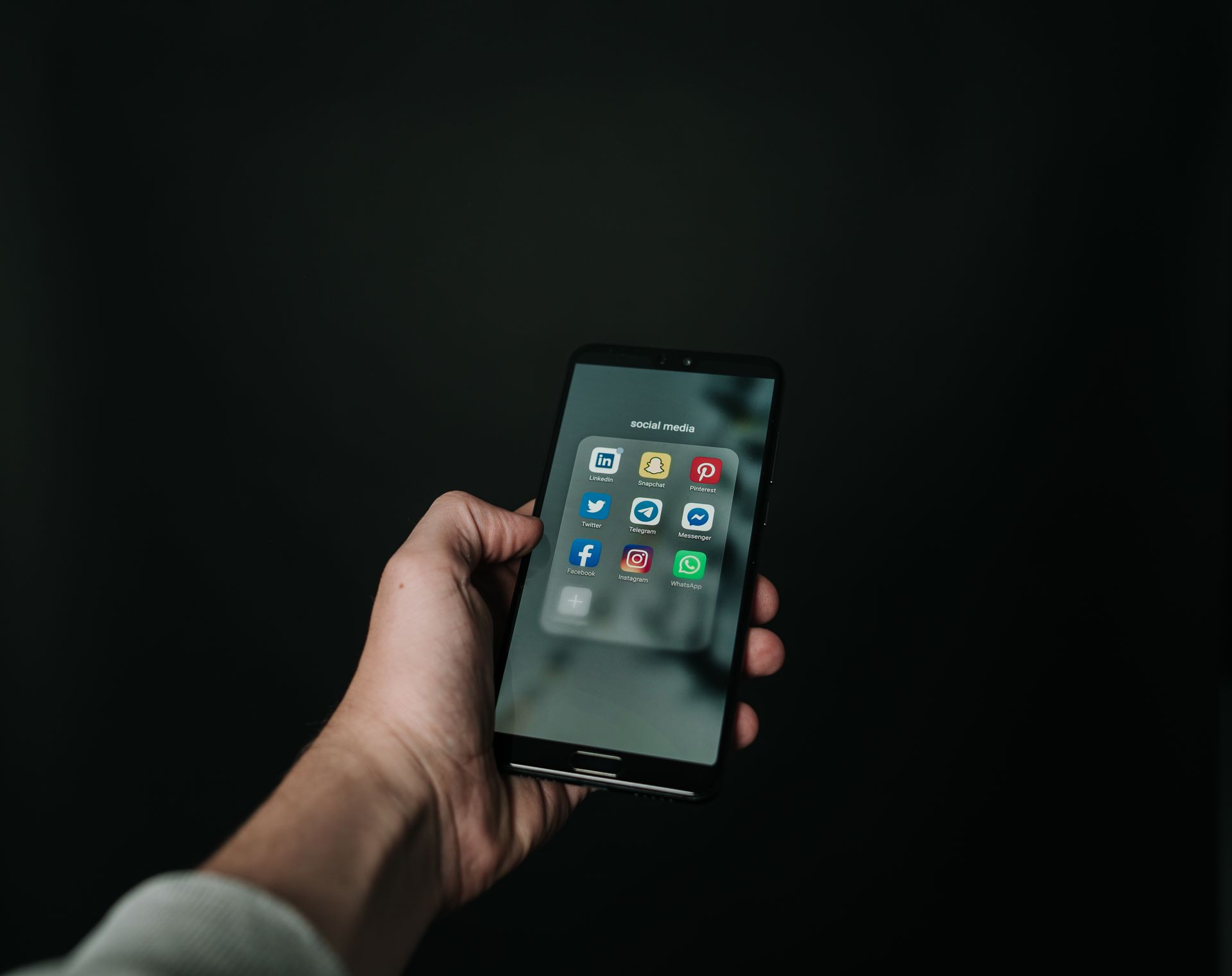 A hand holding a smartphone with a grid of apps on screen against a dark background