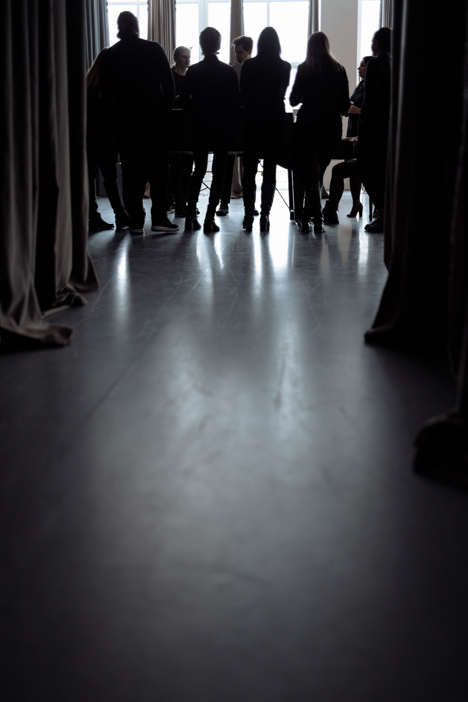 A group of people gathered together in a dim room, silhouetted against bright windows