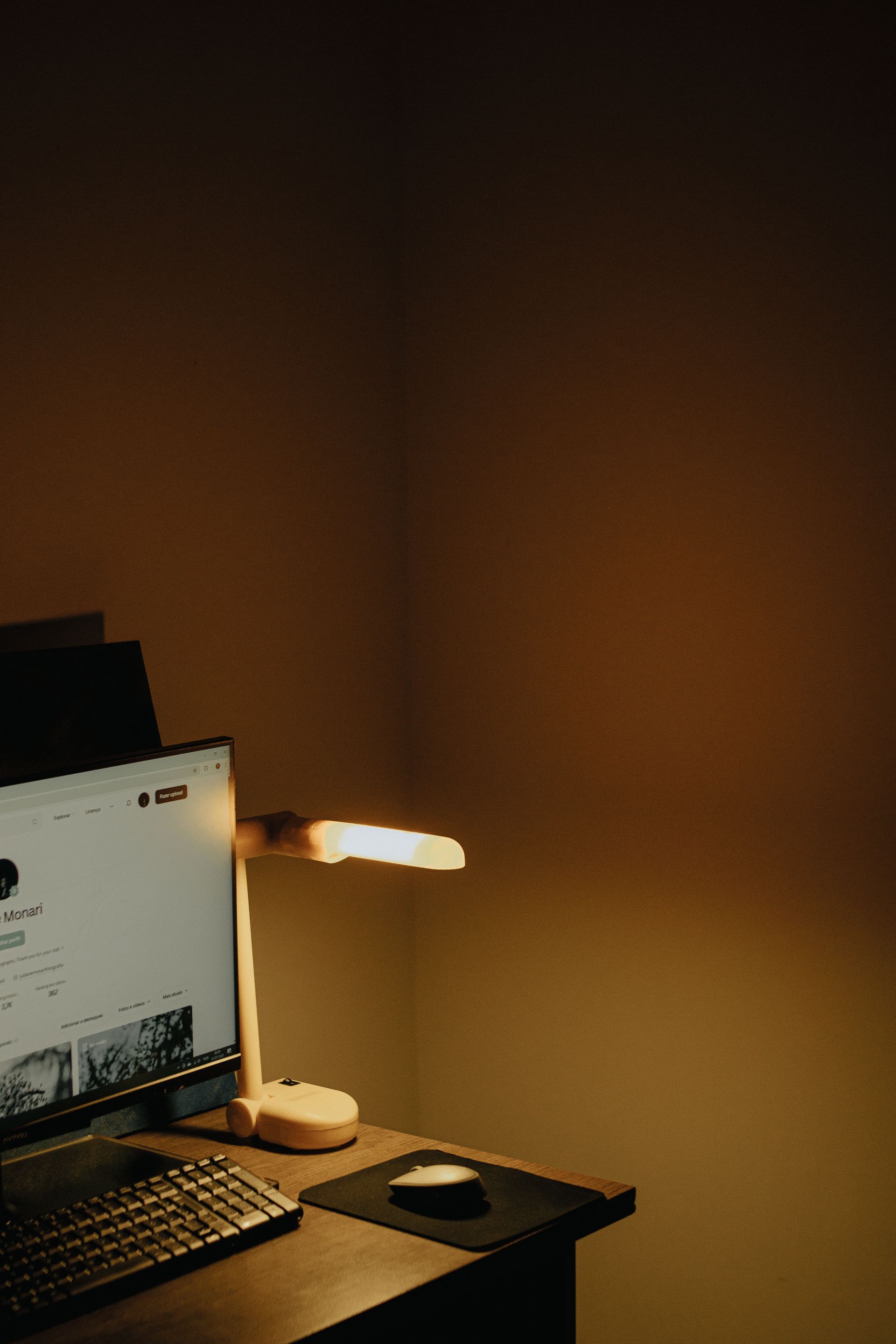 A desk lamp and monitor glowing warm in a dark room, an invitation to sit down and write