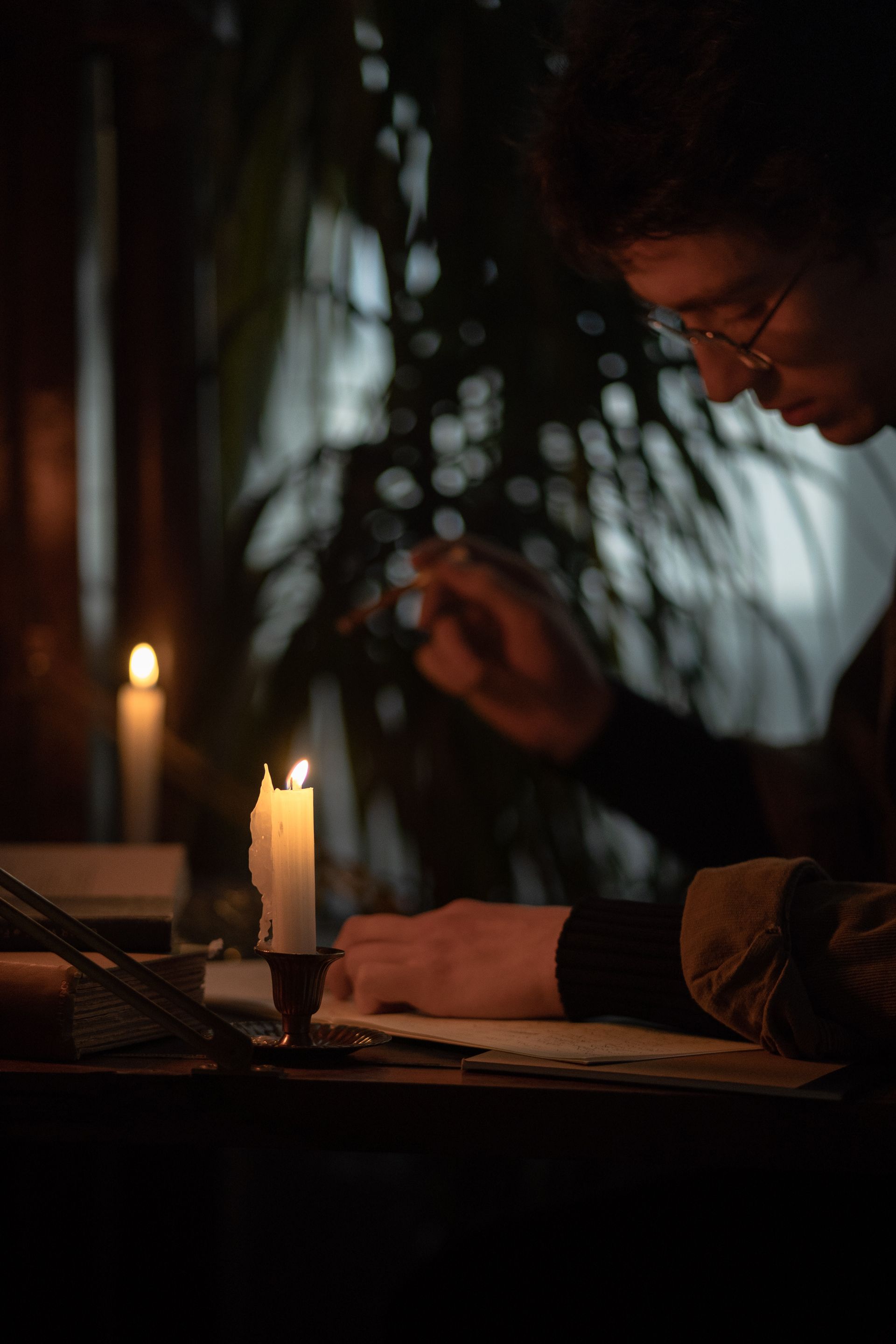 A man writing on paper by candlelight at a dark desk
