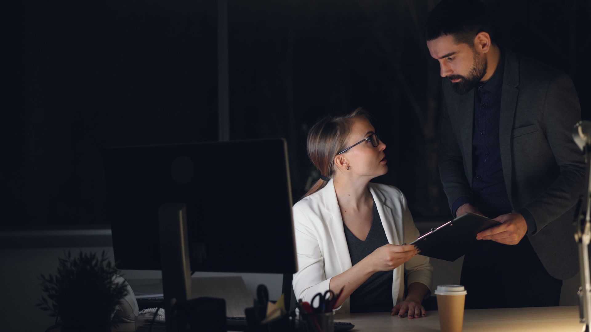 Two colleagues discussing work in a dimly lit office at night