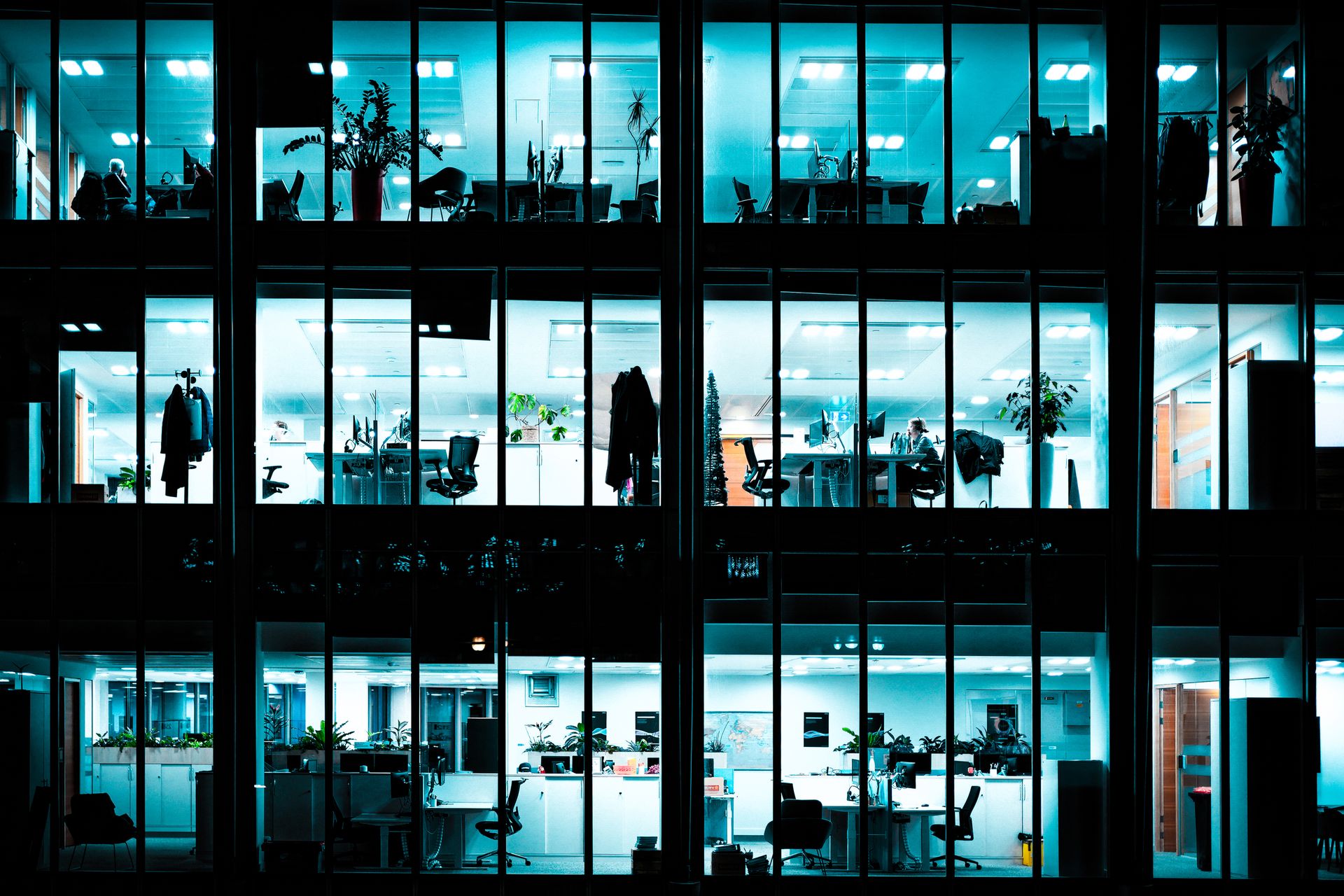 An office building at night, workspaces glowing as pools of light inside the dark structure