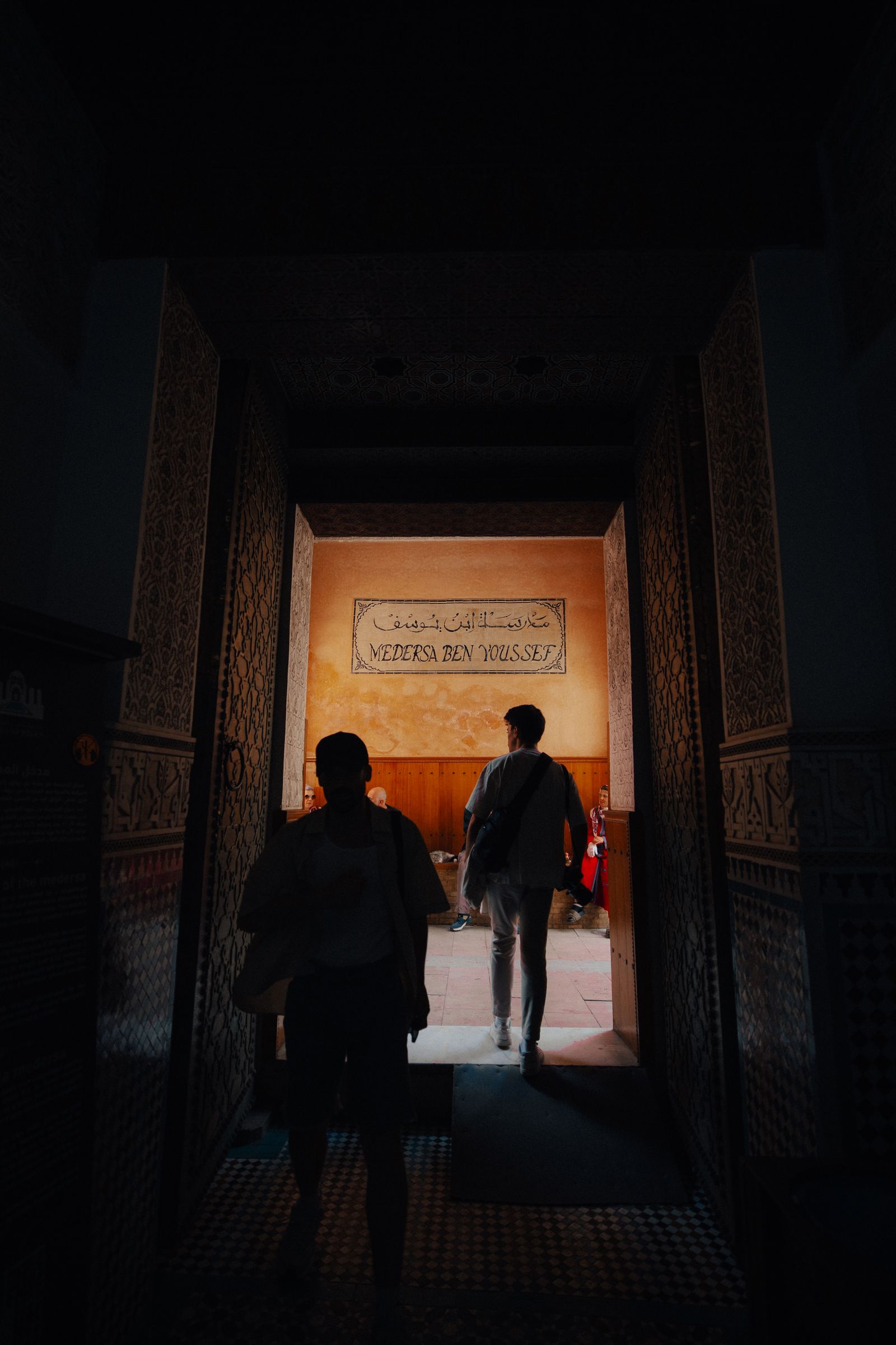 Two silhouetted figures walking through a tall doorway from darkness into warm light